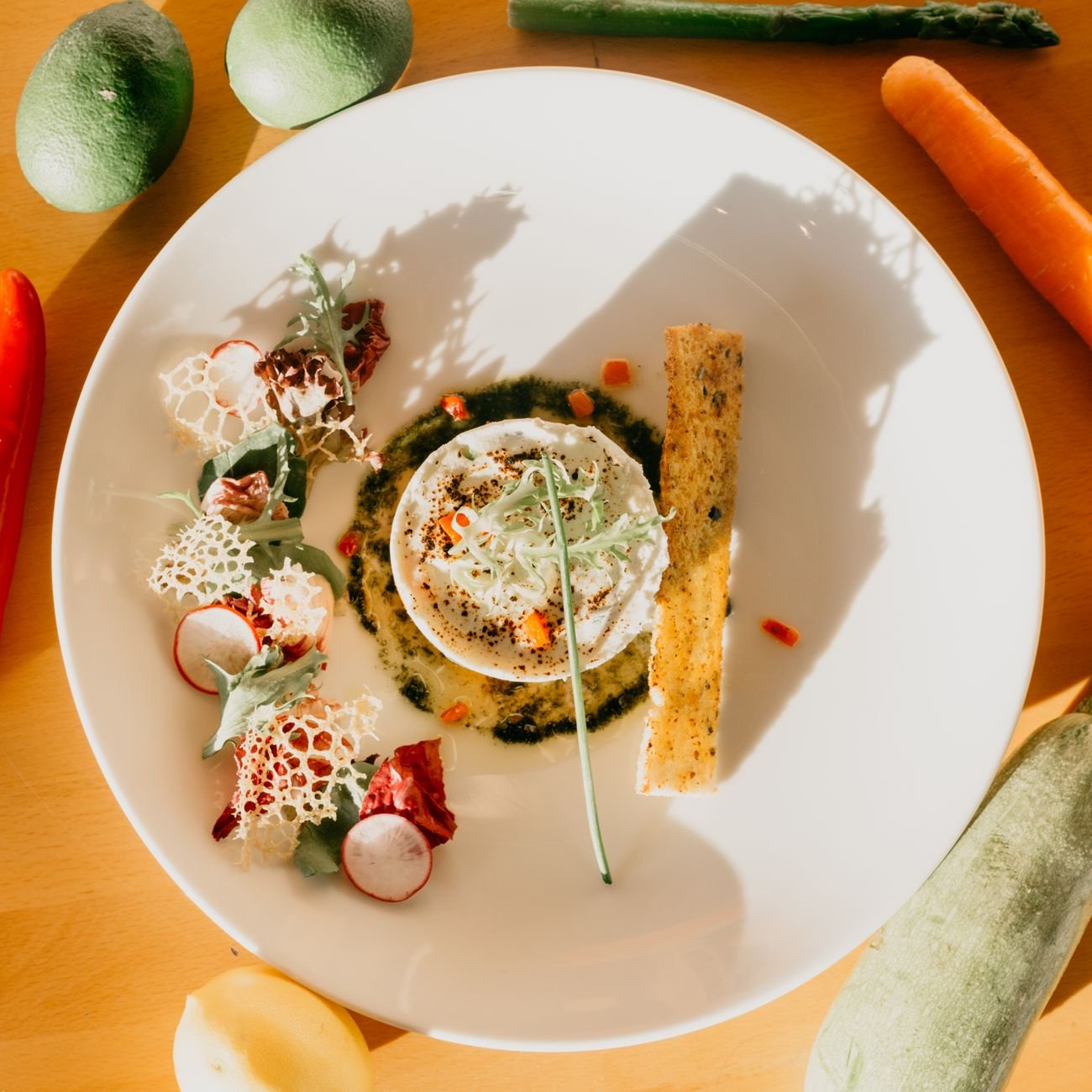 Appetising dish garnished with healthy salad and crispy bread placed on wooden table with assorted vegetables in sunlight
